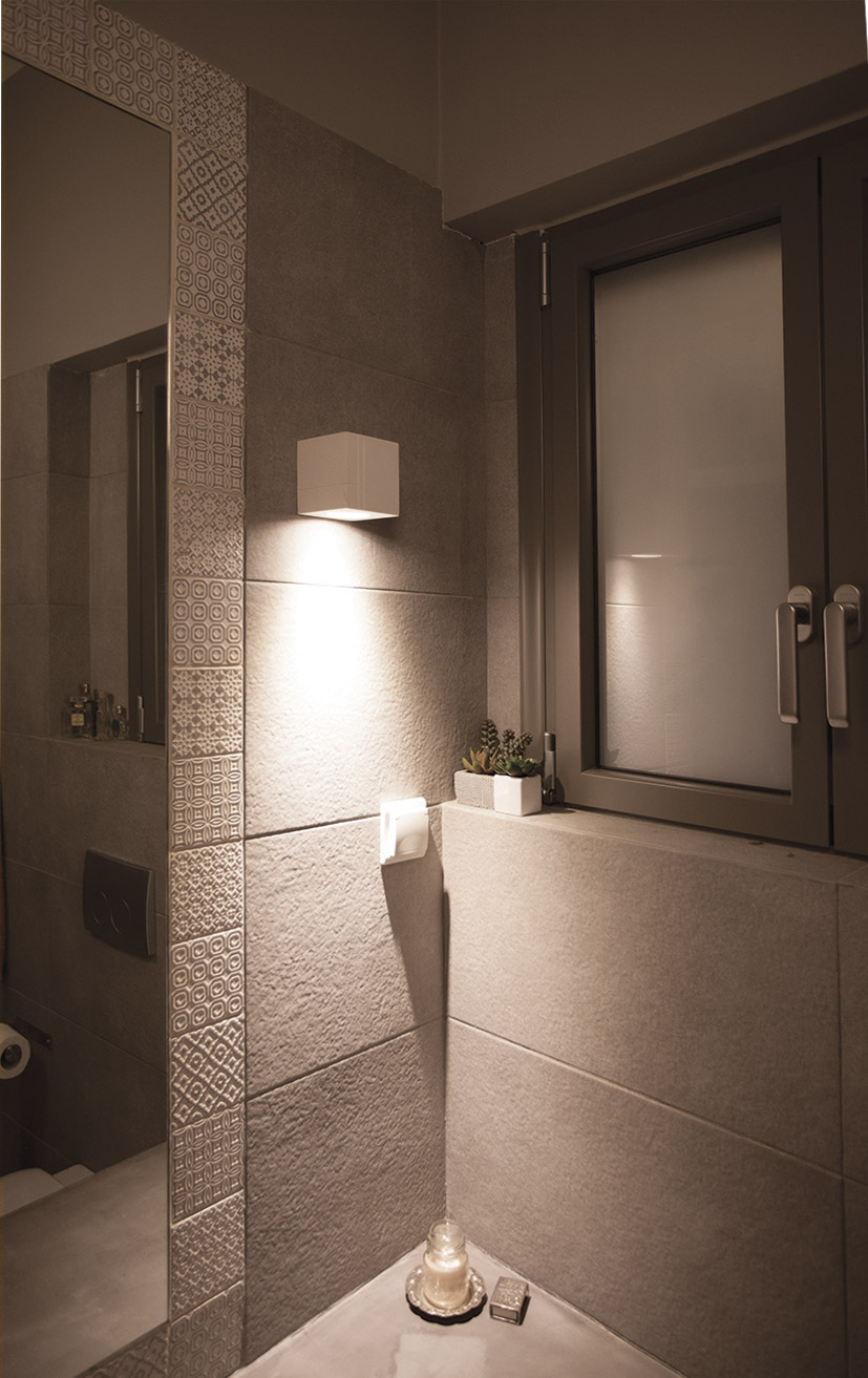 Nama Mondi Down Cube Wall Light lighting down a tiled wall in a contemporary bathroom