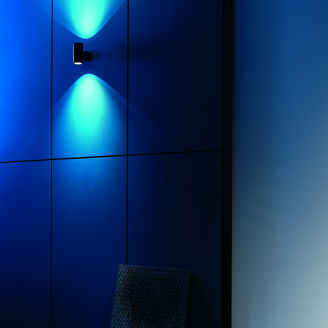 Lifestyle image of the Flexalighting Keller Double Emission wall light illuminating a blue wall outside.