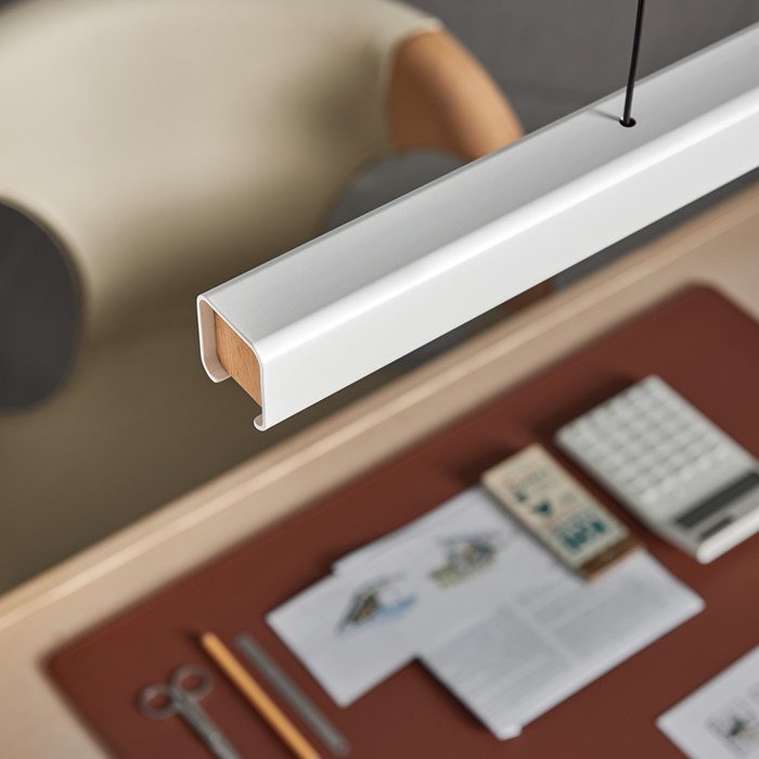Lifestyle shot of the white and beech Mumu P120 Pendant, hanging above a work desk with stationary and paperwork