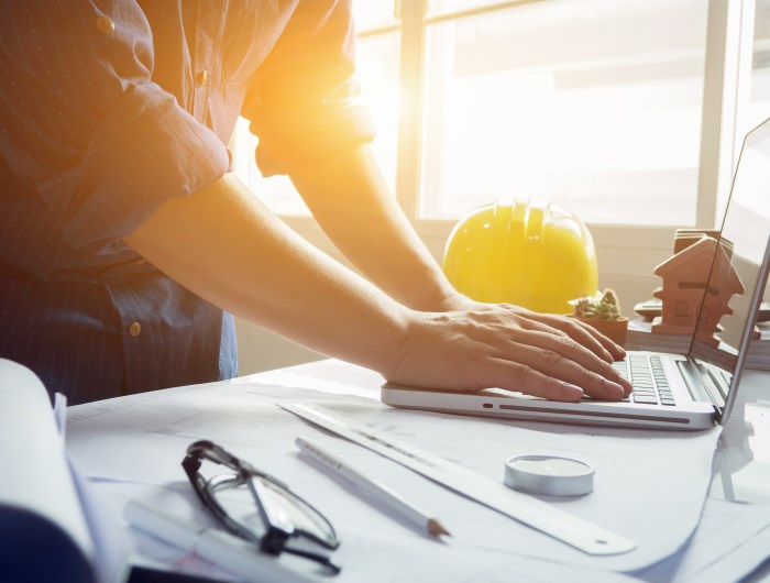 Trade image of an architect or builder with laptop, drawings, hardhat & glasses with sun glare behind