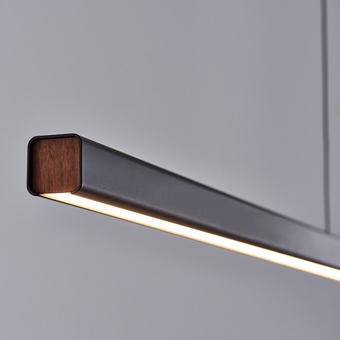Seed Design close up of Mumu Linear LED Pendant in black with walnut detailing, warm light against. grey background