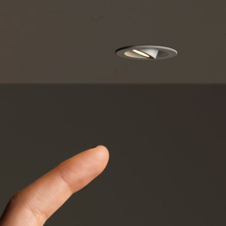 Architectural round LED niche furniture spot light with a finger about to adjust the beam