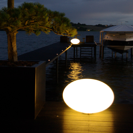 Outdoor table & floor LED lamps lighting a wooden pier on the lake at night