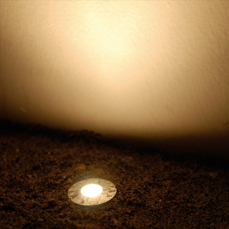 Outdoor recessed round LED uplight installed in the ground & shining a warm white light up a wall