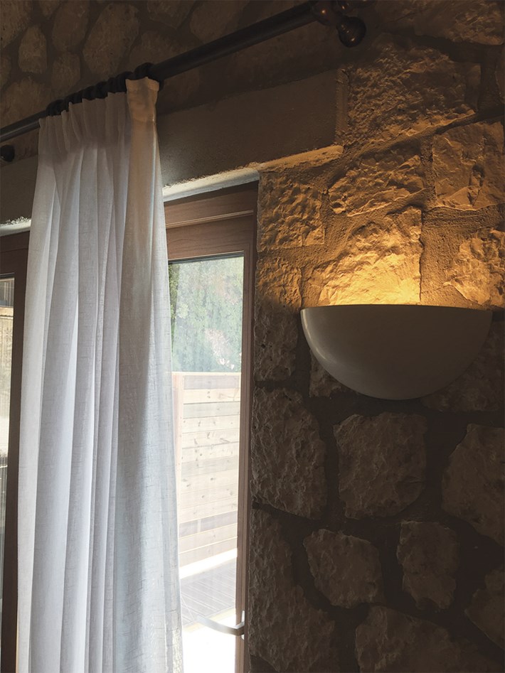 Nama Sfera 01 bowl wall lamp lighting upwards on an indoor rustic stone wall near a window 