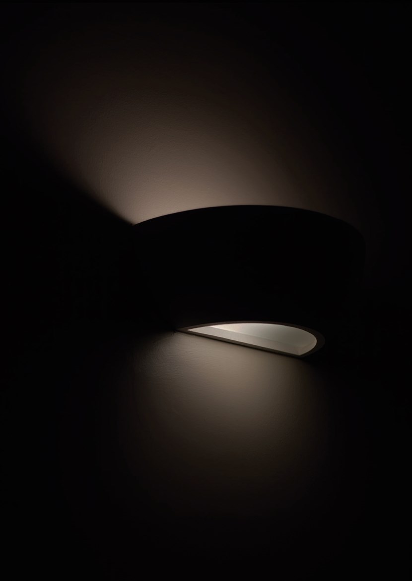 Nama Sfera 02 plaster wall light in silhouette, switched on & lighting up and down a wall at night 