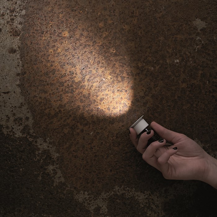 The Flexalighting Hero 6 round downlight in white being held in a hand illuminating a rusty concrete surface.