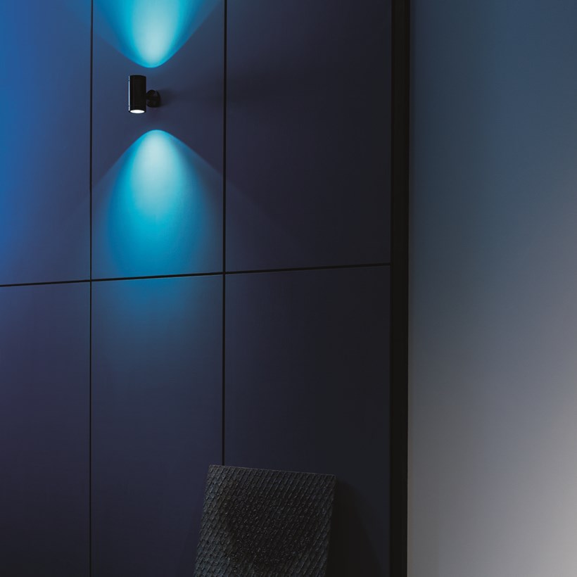 Lifestyle image of the Flexalighting Keller Double Emission wall light illuminating a blue wall outside.