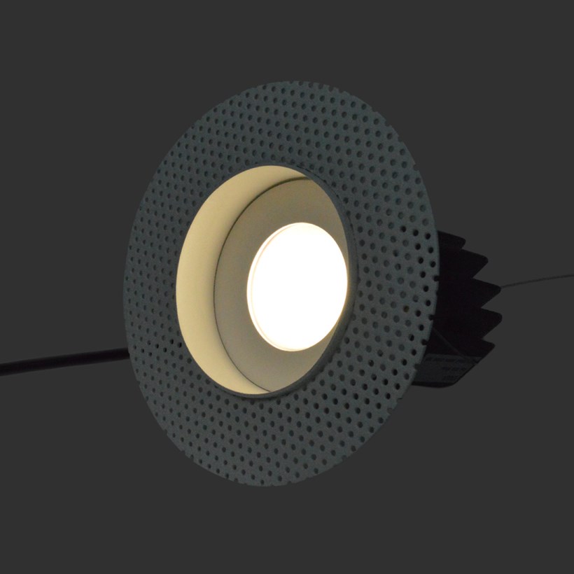 Three quarter view of DLD Eiger Mini True Colour CRI98 LED downlight with plaster-in frame switched on against a dark background