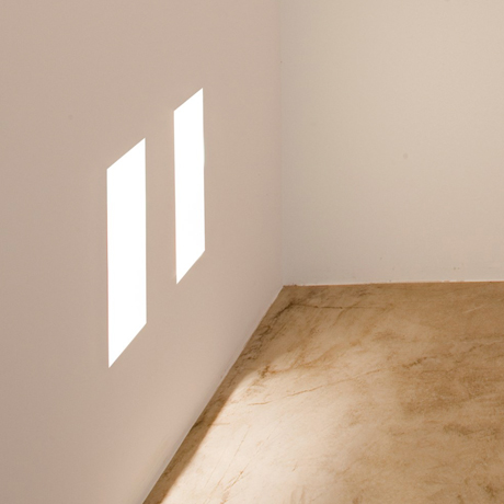 Architectural recessed rectangular low level LED step light plastered into the wall, lighting down onto a travertine marble floor