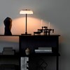 The Nuura Blossi Table Lamp in black, in a roomshot on top of a dark cabinet.