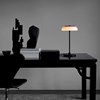 The Nuura Blossi Table Lamp in black, on a dark table in a home study area.