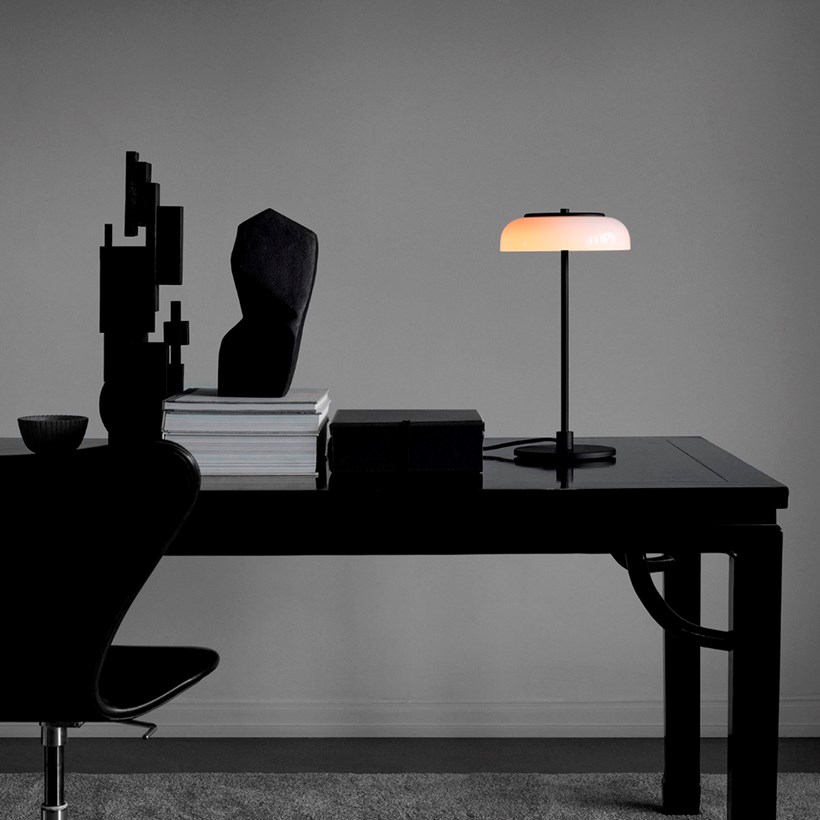 The Nuura Blossi Table Lamp in black, on a dark table in a home study area.