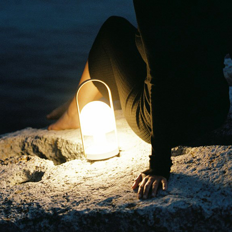 Outdoor portable & cordless LED lamp on a rocky beach next to a man at night with sea view