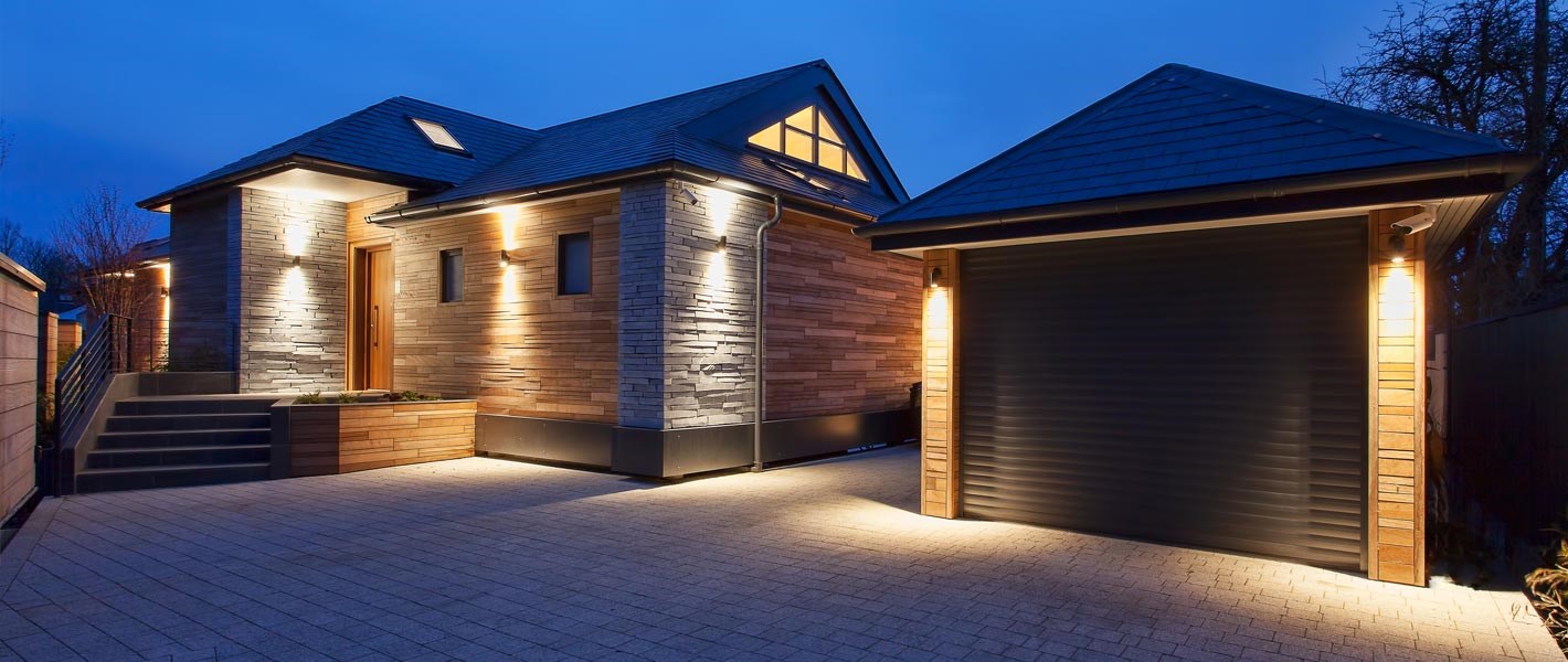 Outdoor shot of a modern home and garage lavishly lit at night with up and down wall lights