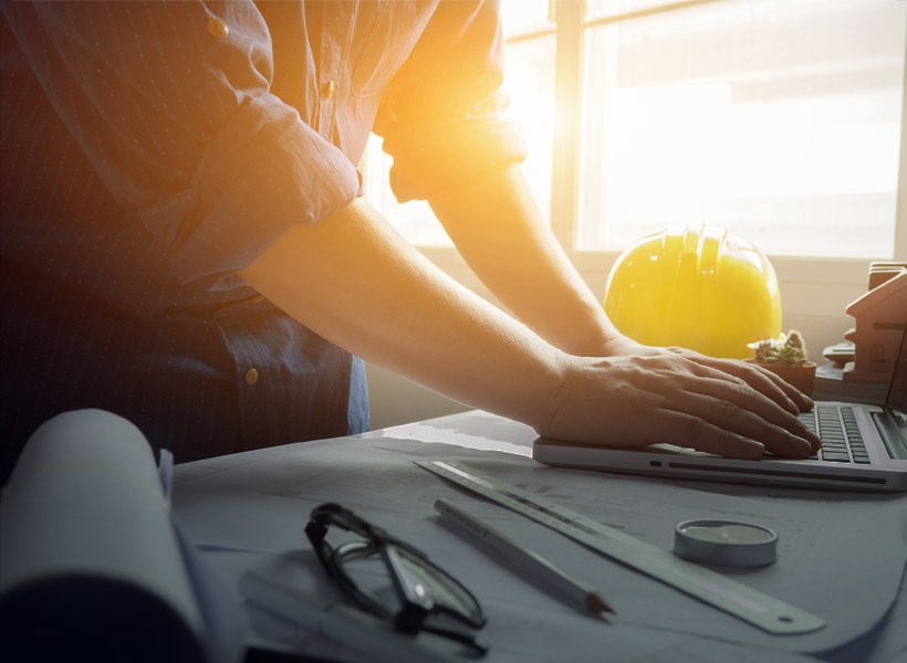 Trade: Image of an architect or builder working on a project with laptop, drawings, hardhat & glasses with sun glare behind