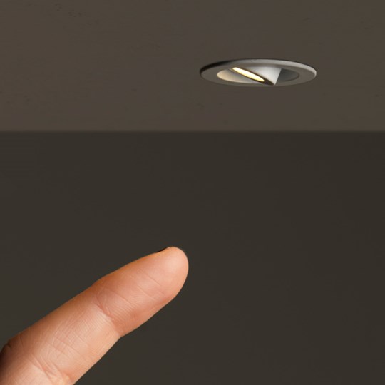 Niche Lighting: Architectural round LED miniature furniture spot light with a finger about to adjust the beam angle
