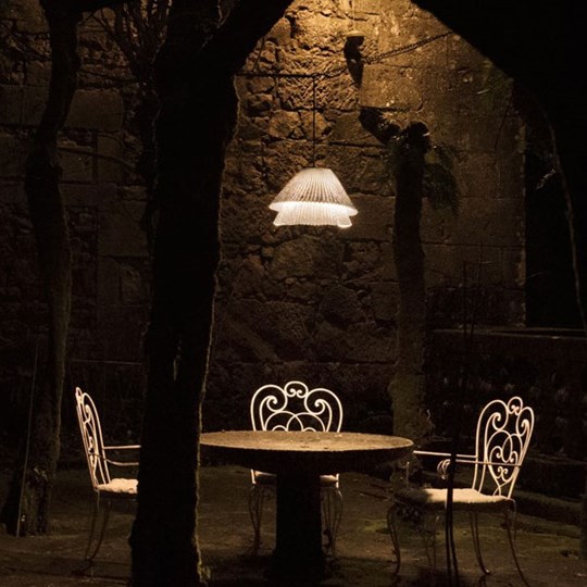 Outdoor LED pendant light suspended over a bistro table & chairs at night