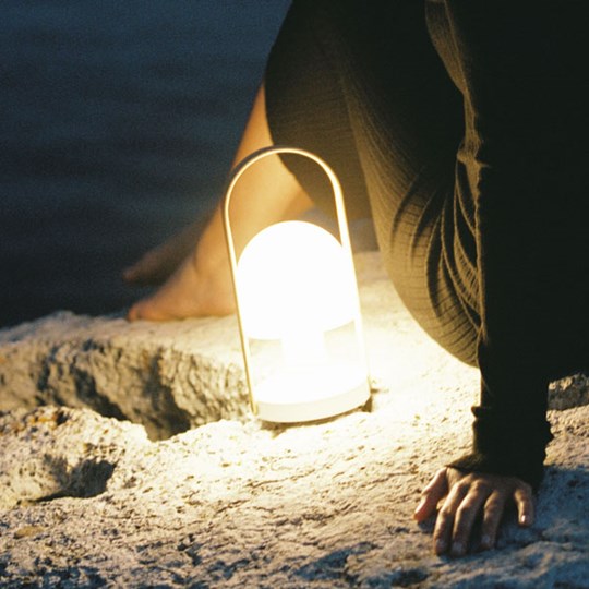 Outdoor portable & cordless LED lamp on a rocky beach next to a man at night with sea view