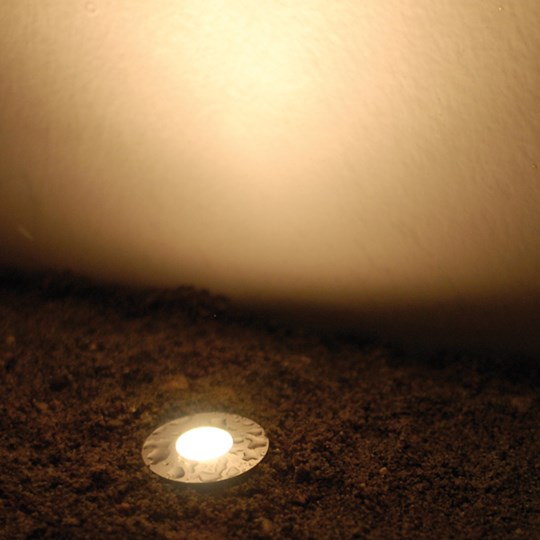 Outdoor recessed round LED uplight installed in the ground & shining a warm white light up a wall