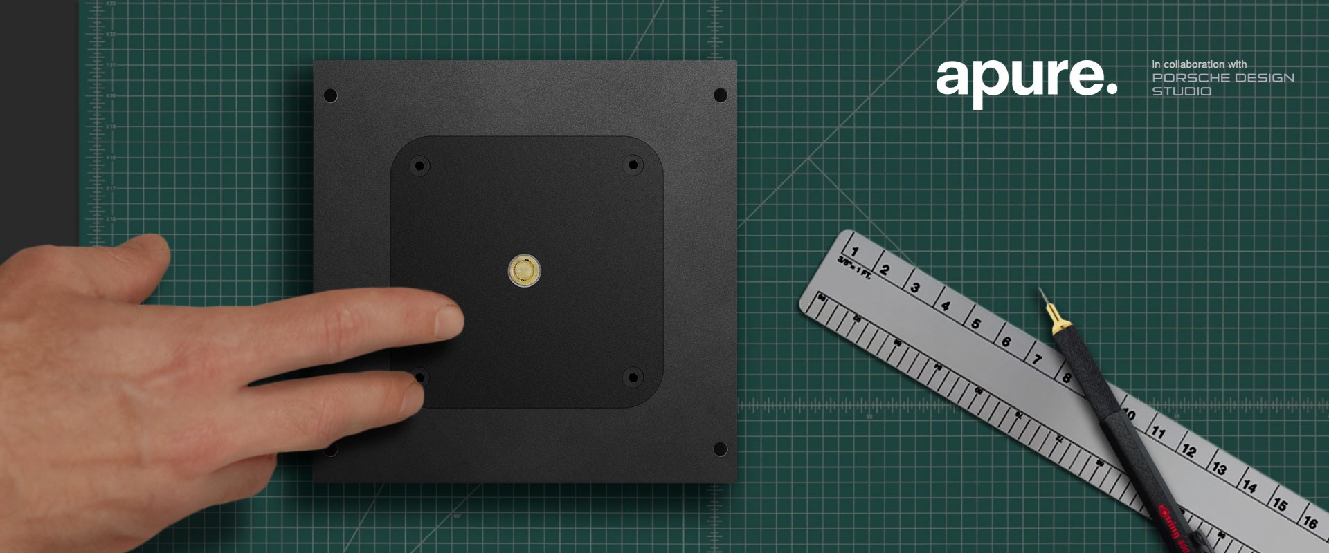 Hand showing the 10mm aperture of the Apure Minus 1 plaster in downlight: architects ruler, drawing pencil & cutting mat to show scale