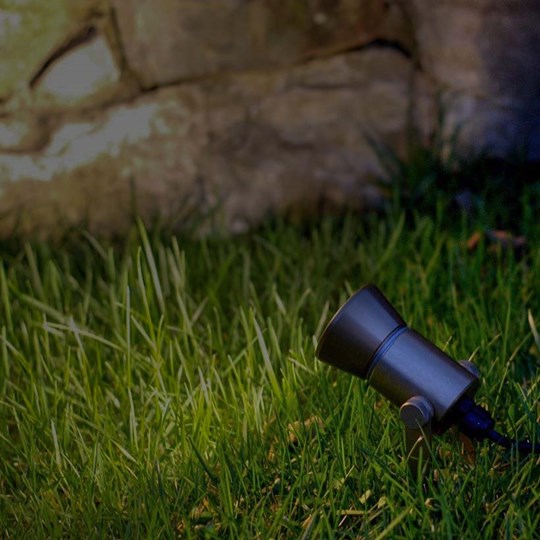 Outdoor Lighting: black adjustable spike spot installed in grass & lighting a rustic stone wall