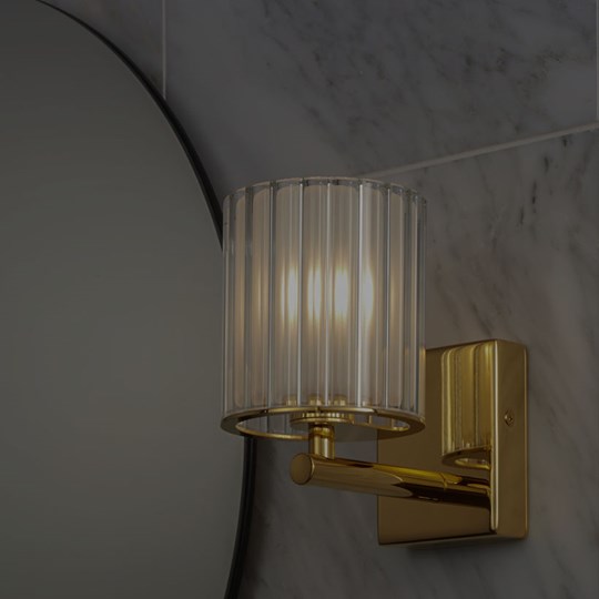 Indoor Lighting: IP rated wall light in gold with glass shade installed in a bathroom next to a round mirror
